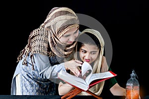 Adorable Pakistani girl with beautiful eyes wear hijab, learning Quran book with mother, Muslim family, daughter and mom read holy