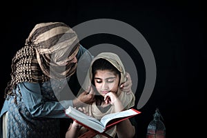 Adorable Pakistani girl with beautiful eyes wear hijab, learning Quran book with mother, Muslim family, daughter and mom read holy