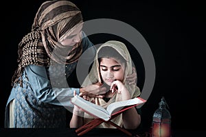 Adorable Pakistani girl with beautiful eyes wear hijab, learning Quran book with mother, Muslim family, daughter and mom read holy