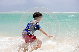 Adorable preschool child, boy, having fun on ocean beach. Excited children playing with waves, swimming, splashing happily,