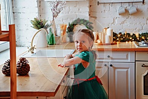 Adorable preschool girl wearing fancy bright green waiting for Christmas in the kitchen.