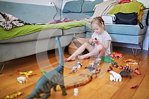 Adorable preschooler girl playing with dinosaurs and toy animals at home