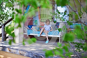 Adorable preschooler girl relaxing on bed with many pillows on a wooden pation of rural house