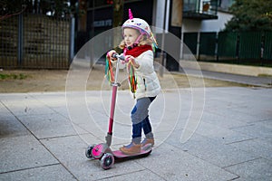 Adorable preschooler girl riding her scooter in a city park on sunny spring day