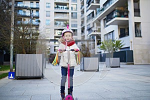 Adorable preschooler girl riding her scooter in a city park on sunny spring day