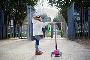 Adorable preschooler girl riding her scooter in a city park on sunny spring day