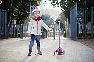 Adorable preschooler girl riding her scooter in a city park on sunny spring day