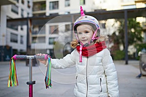 Adorable preschooler girl riding her scooter in a city park on sunny spring day