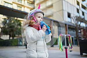 Adorable preschooler girl riding her scooter in a city park on sunny spring day