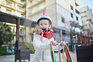 Adorable preschooler girl riding her scooter in a city park on sunny spring day