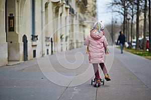 Adorable preschooler girl riding her scooter on a street of Paris, France