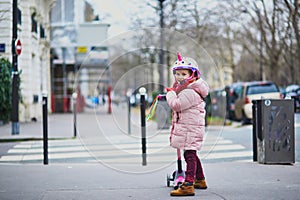 Adorable preschooler girl riding her scooter on a street of Paris, France