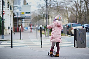 Adorable preschooler girl riding her scooter on a street of Paris, France