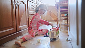 Adorable preschooler girl sitting on the kitchen floor and playing with toy characters at home