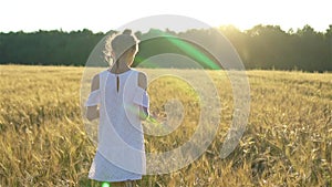 Adorable preschooler girl walking happily in wheat field on warm and sunny summer day