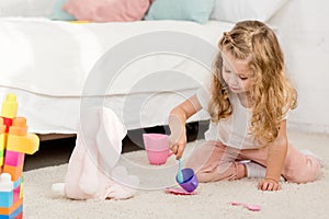 adorable preschooler playing with rabbit toy and plastic cups