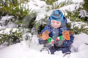 Adorable preschooler in winter wear sit amoung snow and play wit