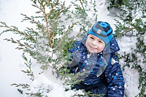 Adorable preschooler in winter wear sit amoung snow and play wit