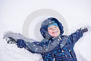 Adorable preschooler in winter wear sit amoung snow and play wit
