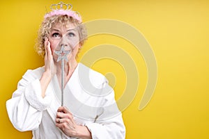 adorable pretty senior lady with magic wand in hands, look up, smile, in white bathrobe