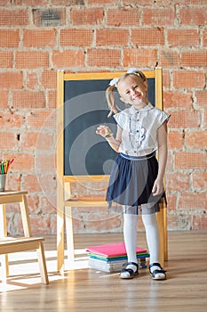 Adorable private schoolgirl in front of blackboard with a bell in her hands