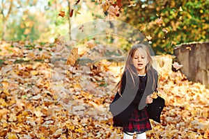 Adorable schoolgirl walking in autumn park after school. Beautiful child girl throwing autumn leaves