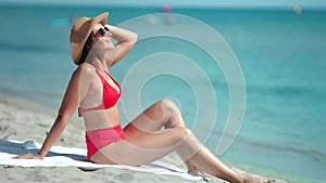 Adorable sexy fashion woman in red swimsuit enjoying sunbathing sitting on sand beach