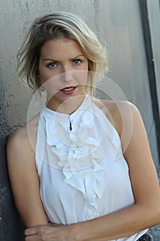 Adorable shapely blond woman in classy white silk blouse posing on gray background