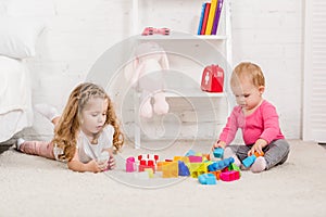 adorable sisters playing with constructor on carpet