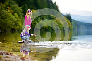 Adorable sisters playing by Hallstatter See lake in Austria on warm summer day. Cute children having fun splashing water and throw photo
