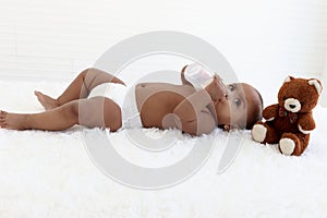 Adorable a sixmonth crawling African American baby lying on fluffy white rug, happy sweet little girl kid holding milk bottle and