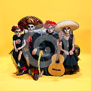 Adorable skeleton posing on yellow background. Happy mexicans family, parents and childrens with creative spooky makeup