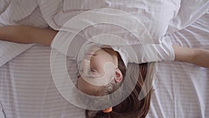 Adorable small girl sleeping in the bed at home. Girl waking up from an alarm clock on her smart watch. Modern