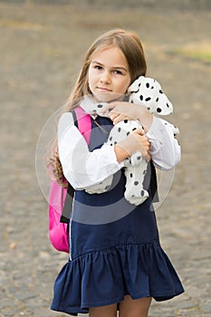 Adorable small kid cuddle cute toy dog wearing school uniform backpack outdoors, afterschool