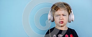 Adorable small three years old boy with cute face expression listening to the music with big white headphones