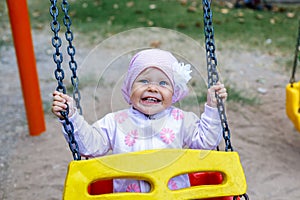 Adorable smiling baby girl with kerchief enjoying a swing ride on a playground in a park on a nice sunny summer day