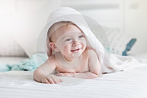 Adorable smiling baby in hooded towel ling on bed after having b