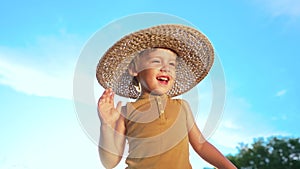 Adorable smiling boy in straw hat on blue sky background. Funny child with kind face looking to camera, enjoying summer