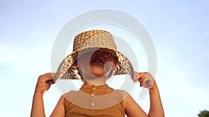 Adorable smiling boy in straw hat on blue sky background. Funny child with kind face looking to camera, enjoying summer