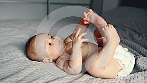 Adorable smiling caucasian 6 months old baby boy holding his feets and looking at camera while lying on bed