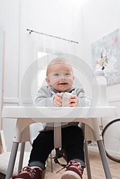 Adorable smiling child sitting in a baby chair in the kitchen and holding baby