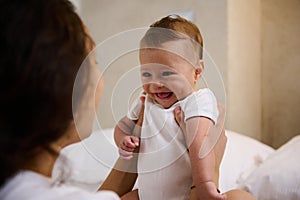 Adorable smiling newborn baby boy in tender embrace of his loving caring mother. Babyhood and infancy concept