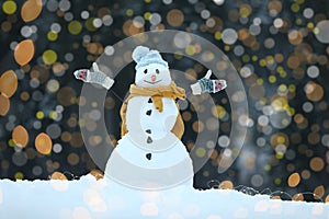 Adorable smiling snowman and blurred Christmas lights on background outdoors.
