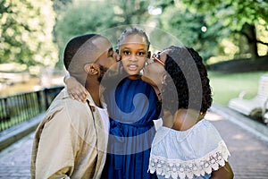 Adorable summer portrait of young african family of three posing together outdoors in beautiful park. Lovely parents are