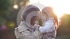 An adorable, sweet little girl hugs her young mother during a walk in a spring park.