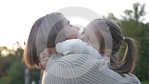 An adorable, sweet little girl hugs her young mother during a walk in a spring park.