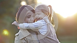 An adorable, sweet little girl hugs her young mother during a walk in a spring park.