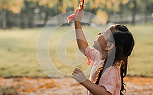 Adorable sweet little girl playing outdoor park alone with sunlight in evening, holding piece of watermelon and looking