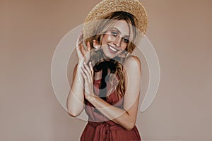 Adorable tanned girl in canotier posing on brown background. Studio shot of smiling gorgeous blonde lady in straw hat..