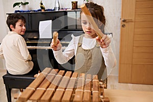 Adorable teen boy and little girl enjoy playing together on musical instruments, perform melody on xylophone and piano